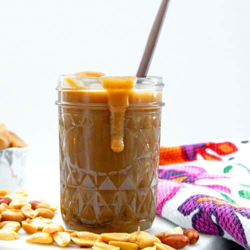 Closeup head-on view of peanut butter syrup dripping down side of a jar with a spoon in it.