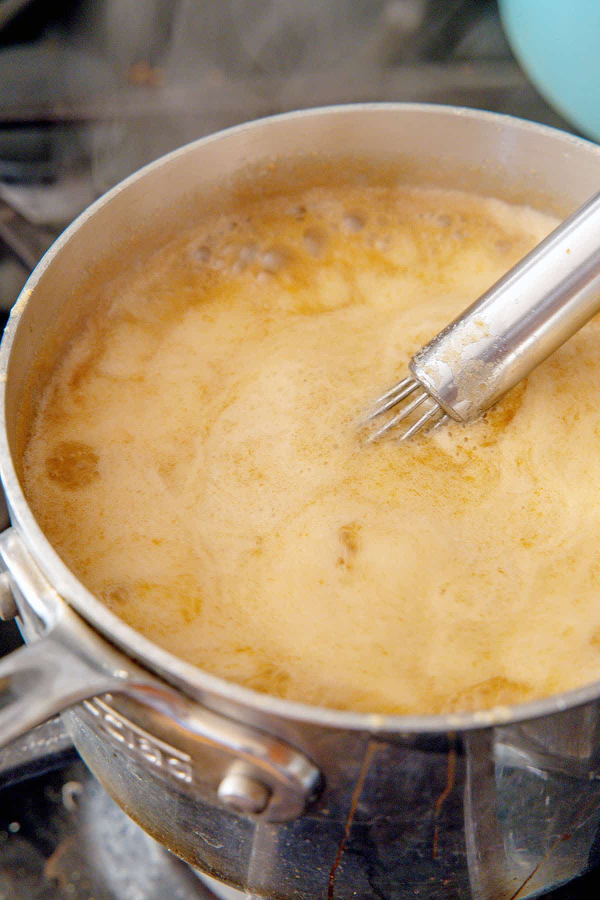Peanut butter syrup simmering in a saucepan with a whisk.