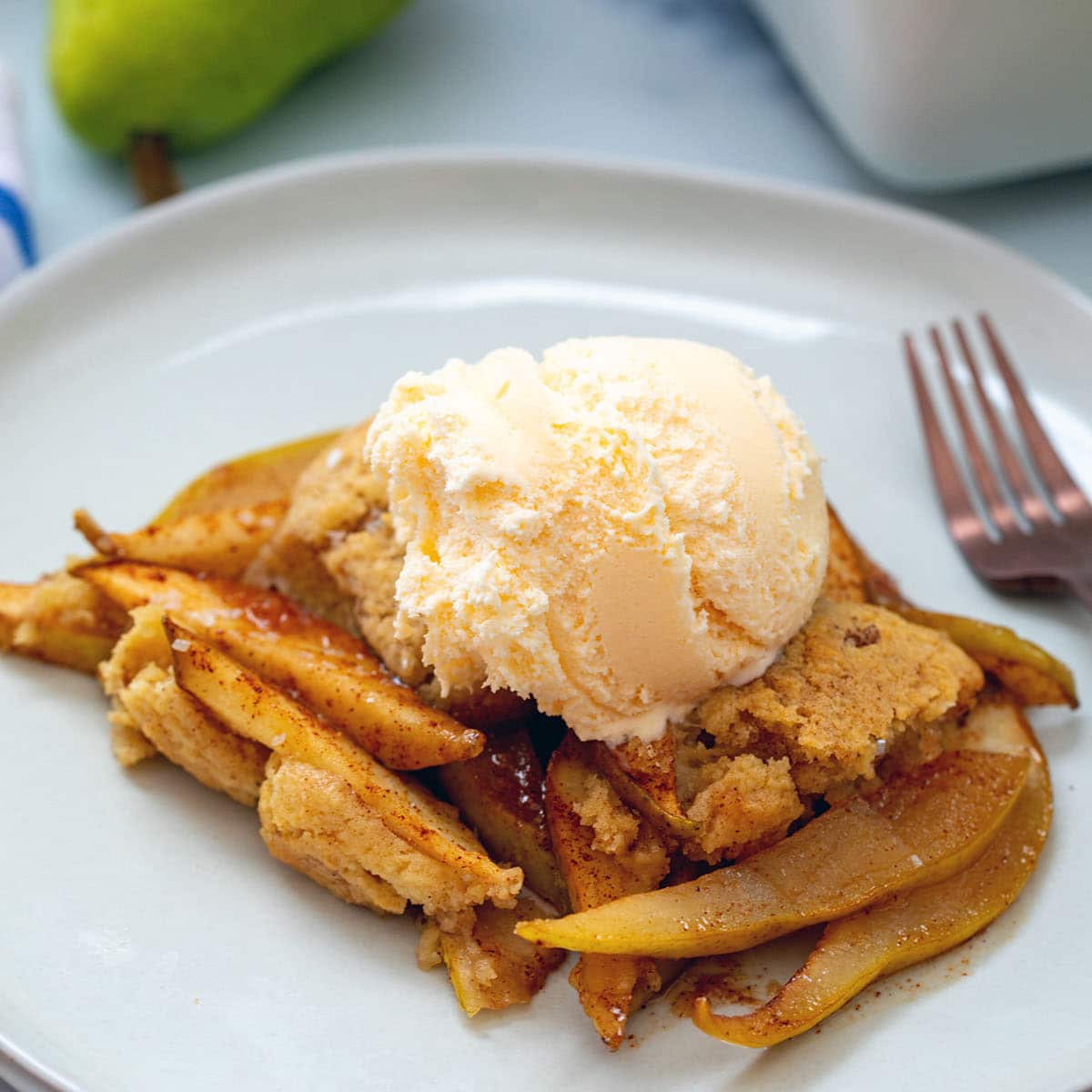 Closeup view of pear cobbler on a plate topped with vanilla ice cream.