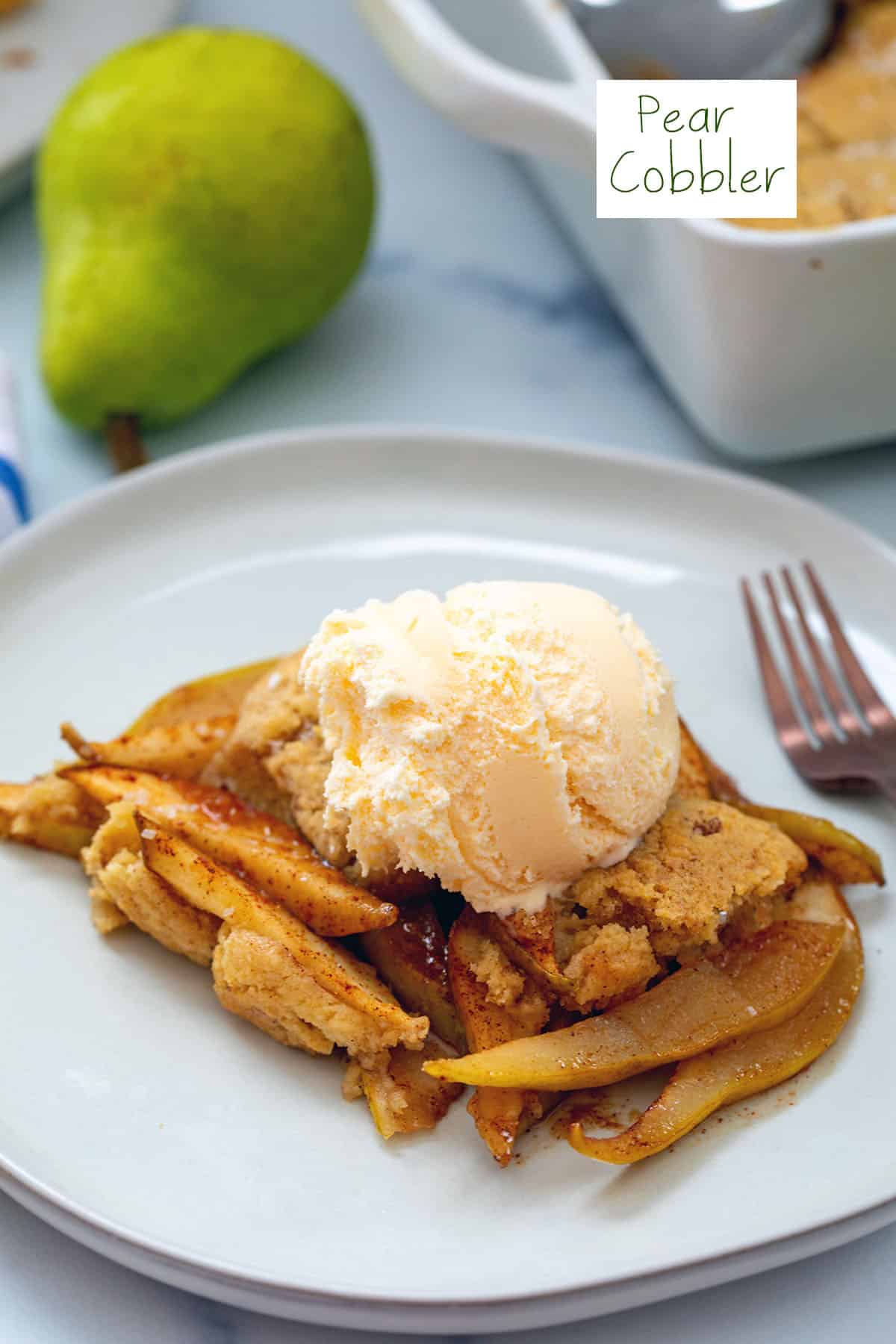 Pear cobbler on a plate topped with vanilla ice cream with pear and baking dish in background and recipe title on top.