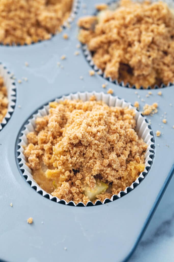 Pear muffin batter topped with crumb topping in muffin tin.