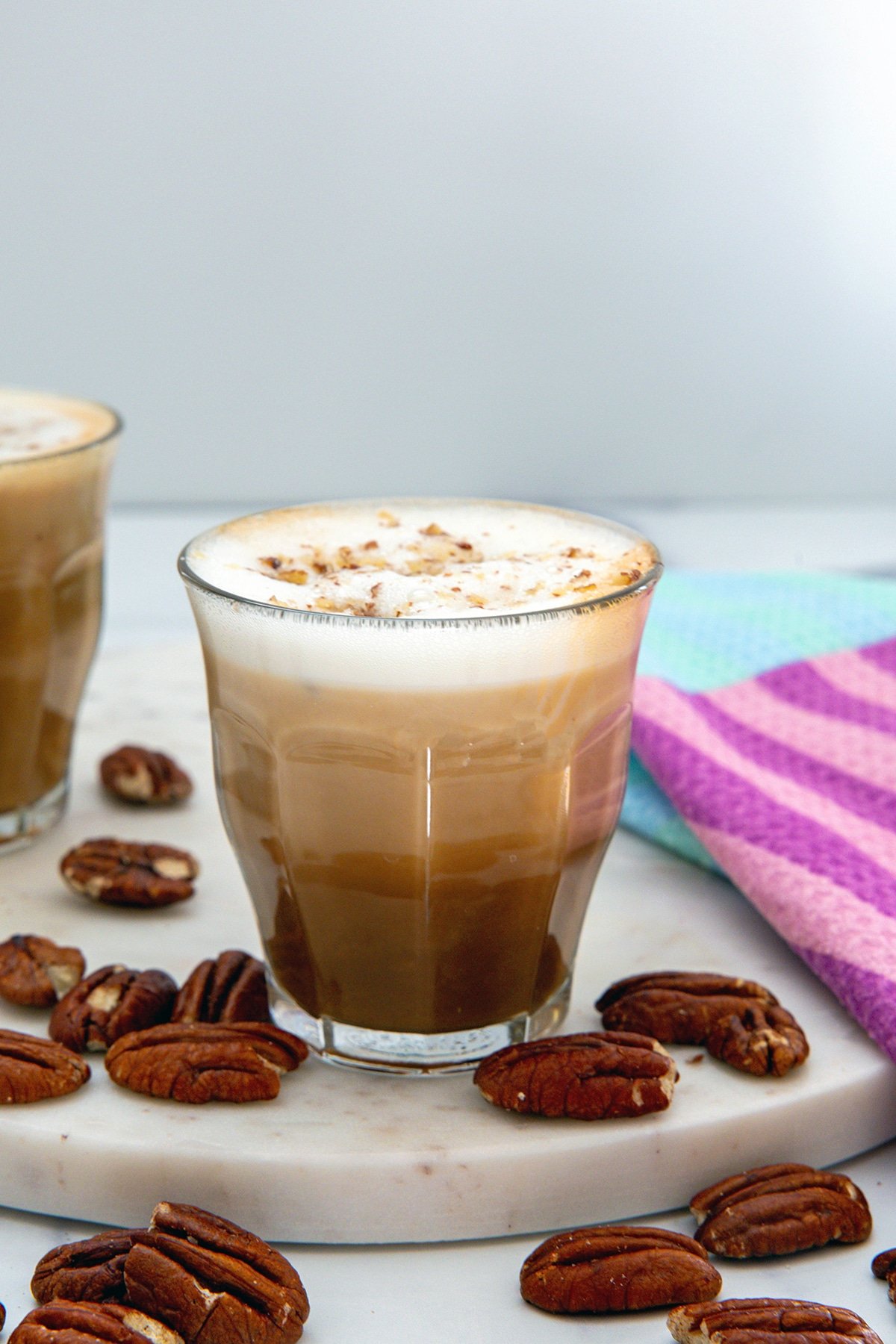 Head-on view of a Pecan Oatmilk Cortado in a small glass with pecans all around.
