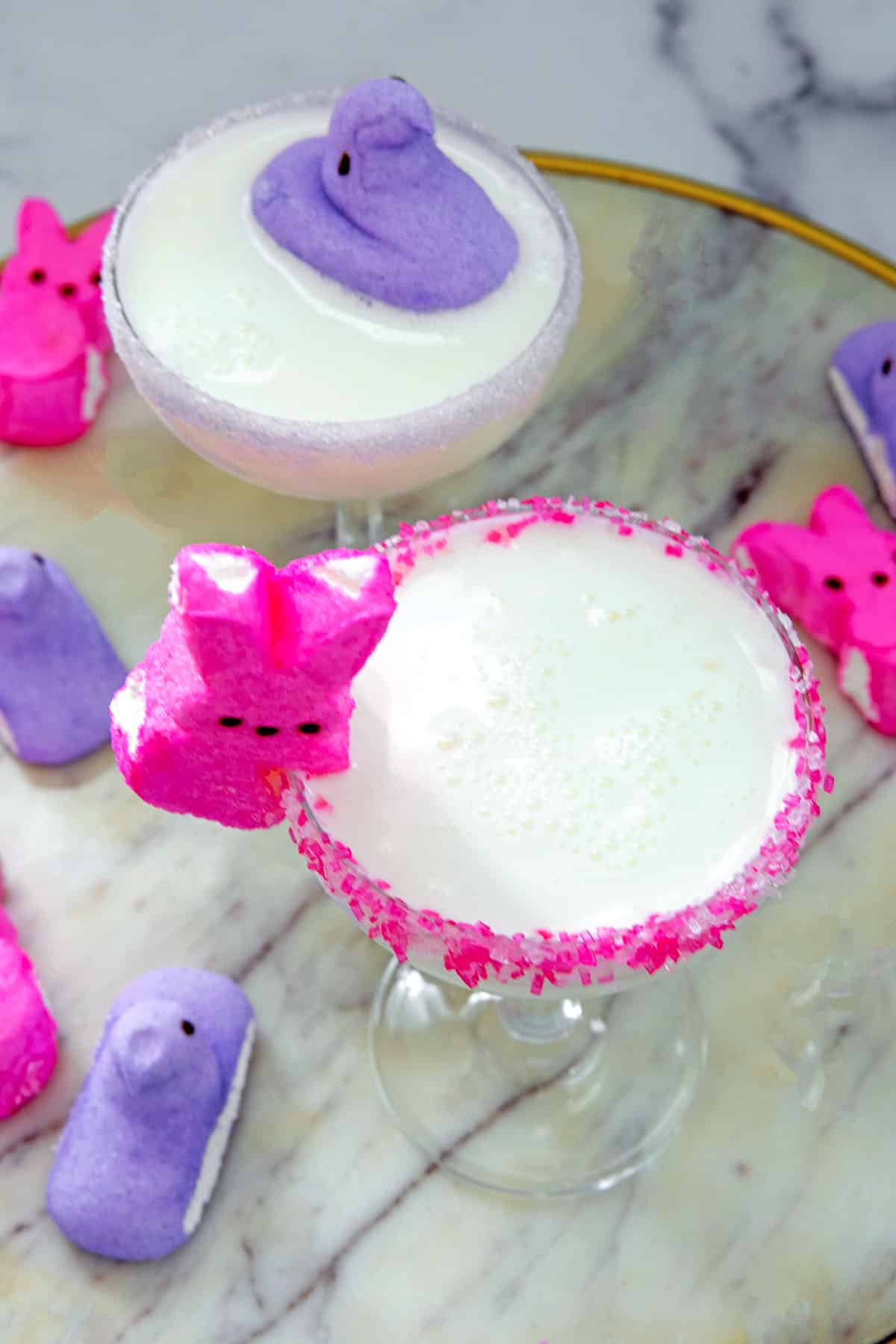 Overhead view of white Peeps martini in coupe glass with sugar rims and pink and purple bunny and chick Peeps all around.