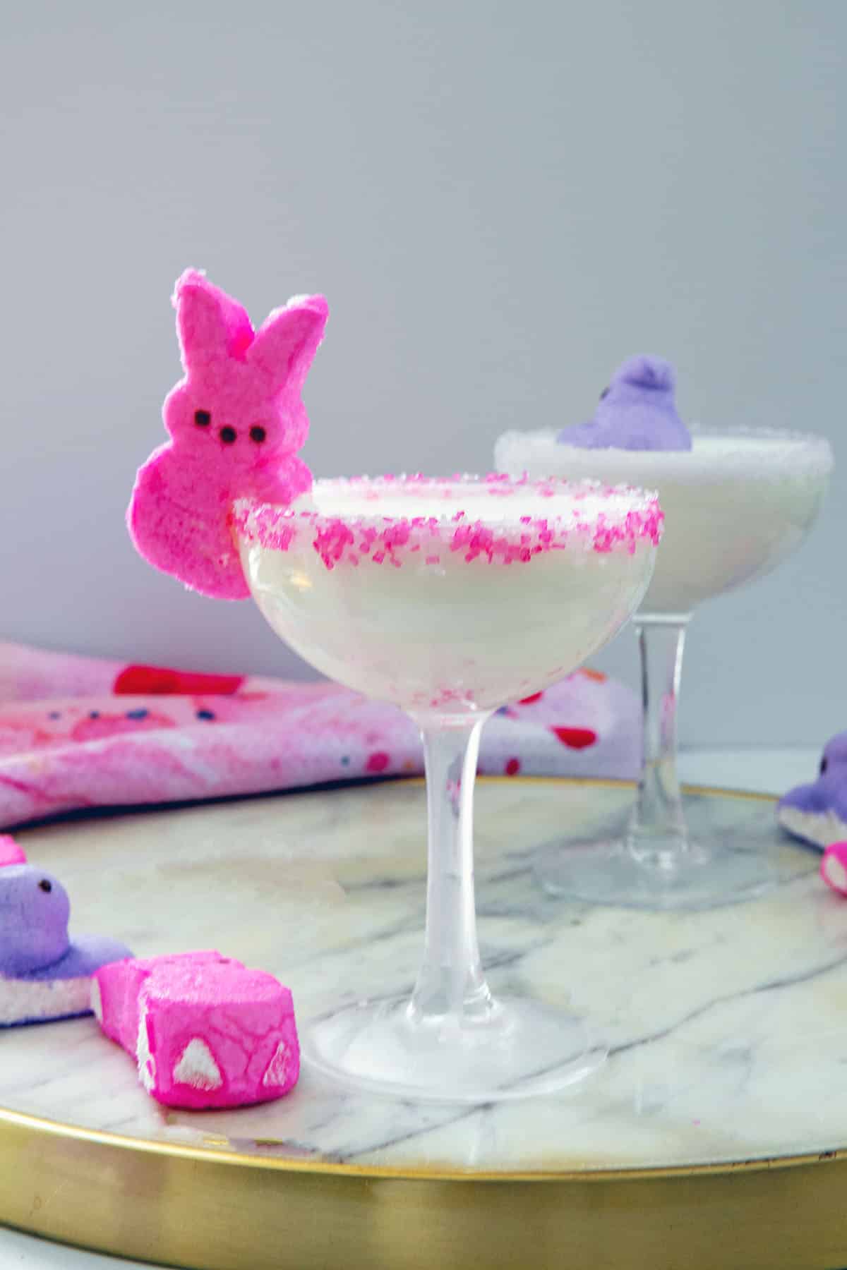 Head-on view of a white cocktail in a coupe glass with pink bunny Peeps on the side with second cocktail in background.