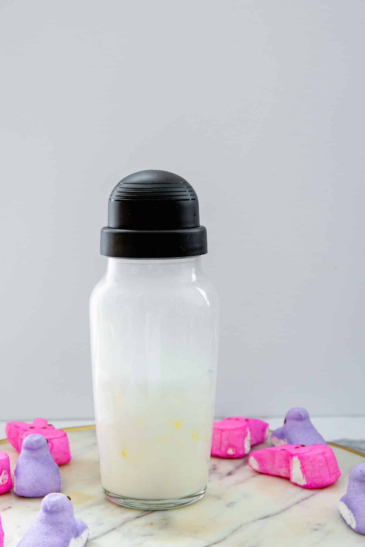 Head-on view of a clear shaker bottle with white cocktail with pink and purple Peeps all around.