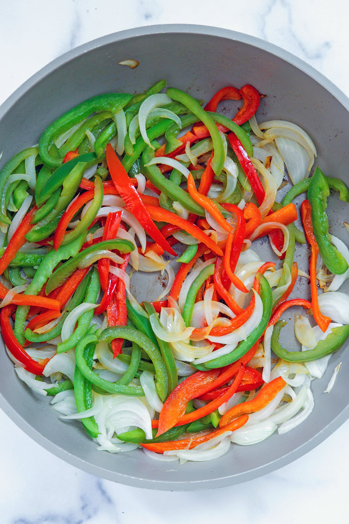 Green and red peppers cooking with onions in skillet.