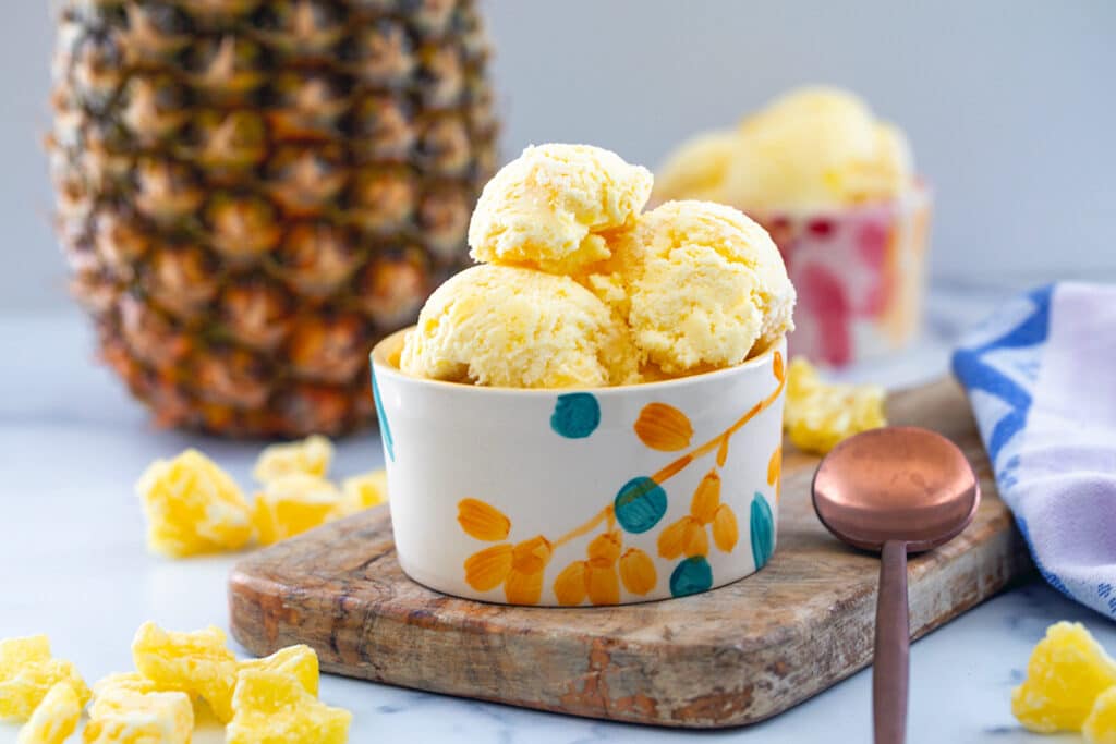 Landscape view of two bowls of pineapple ice cream with fresh pineapple in background.