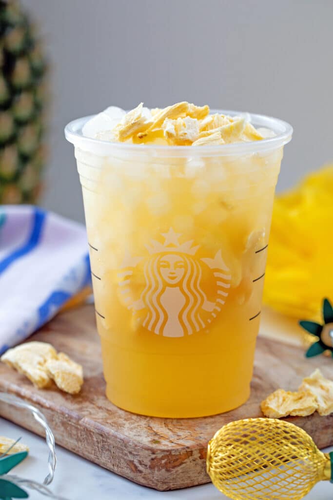 Pineapple Passionfruit Refresher in Starbucks cup with freeze-dried pineapple pieces around.