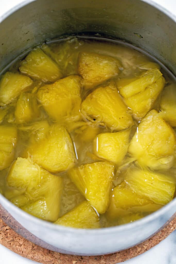Chopped pineapple simmering in water and sugar in saucepan.