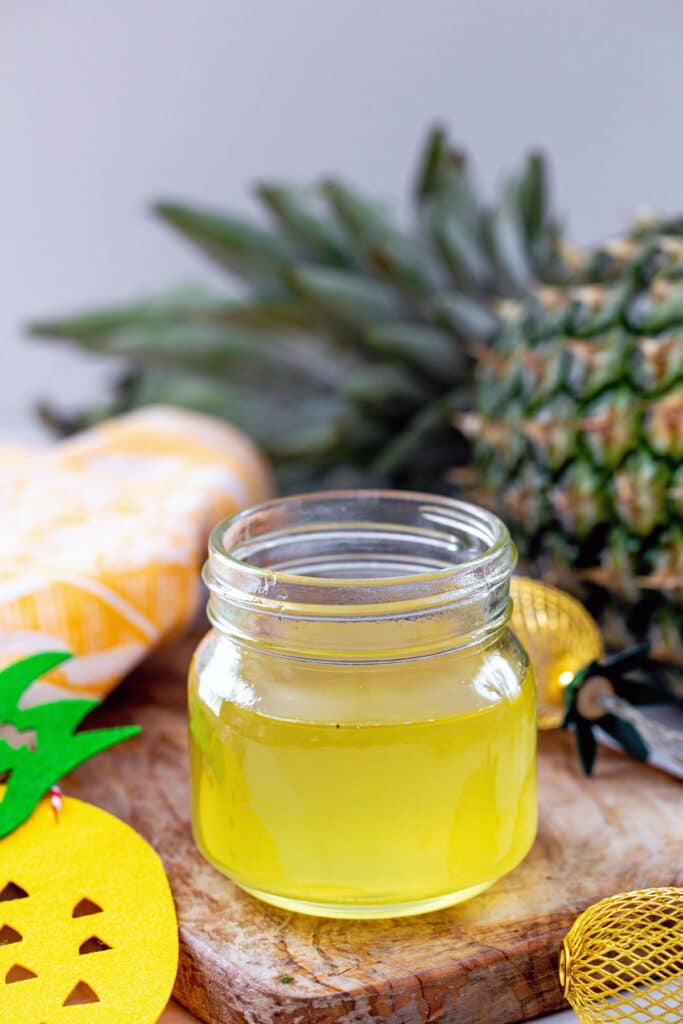 Close-up of a small mason jar of pineapple syrup with fresh pineapple in background.