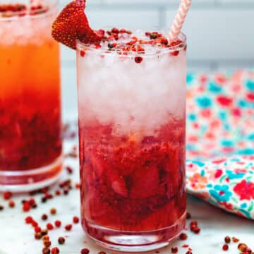 Closeup view of a mashed strawberry cocktail with pink peppercorn garnish.