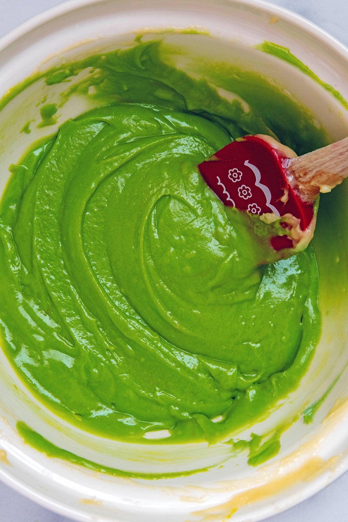 Green pistachio batter in mixing bowl with rubber spatula.