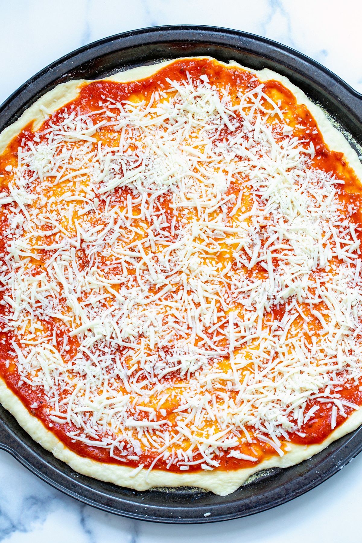Pizza dough rolled on pan with tomato sauce and shredded cheese.