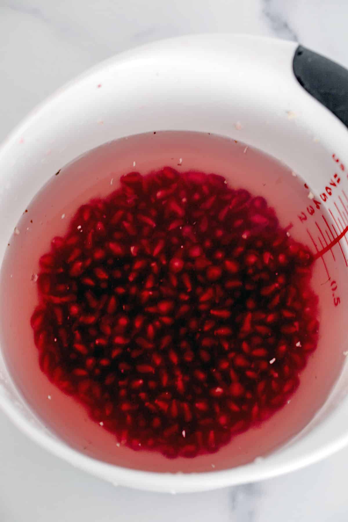 Pomegranate arils in bowl with water.