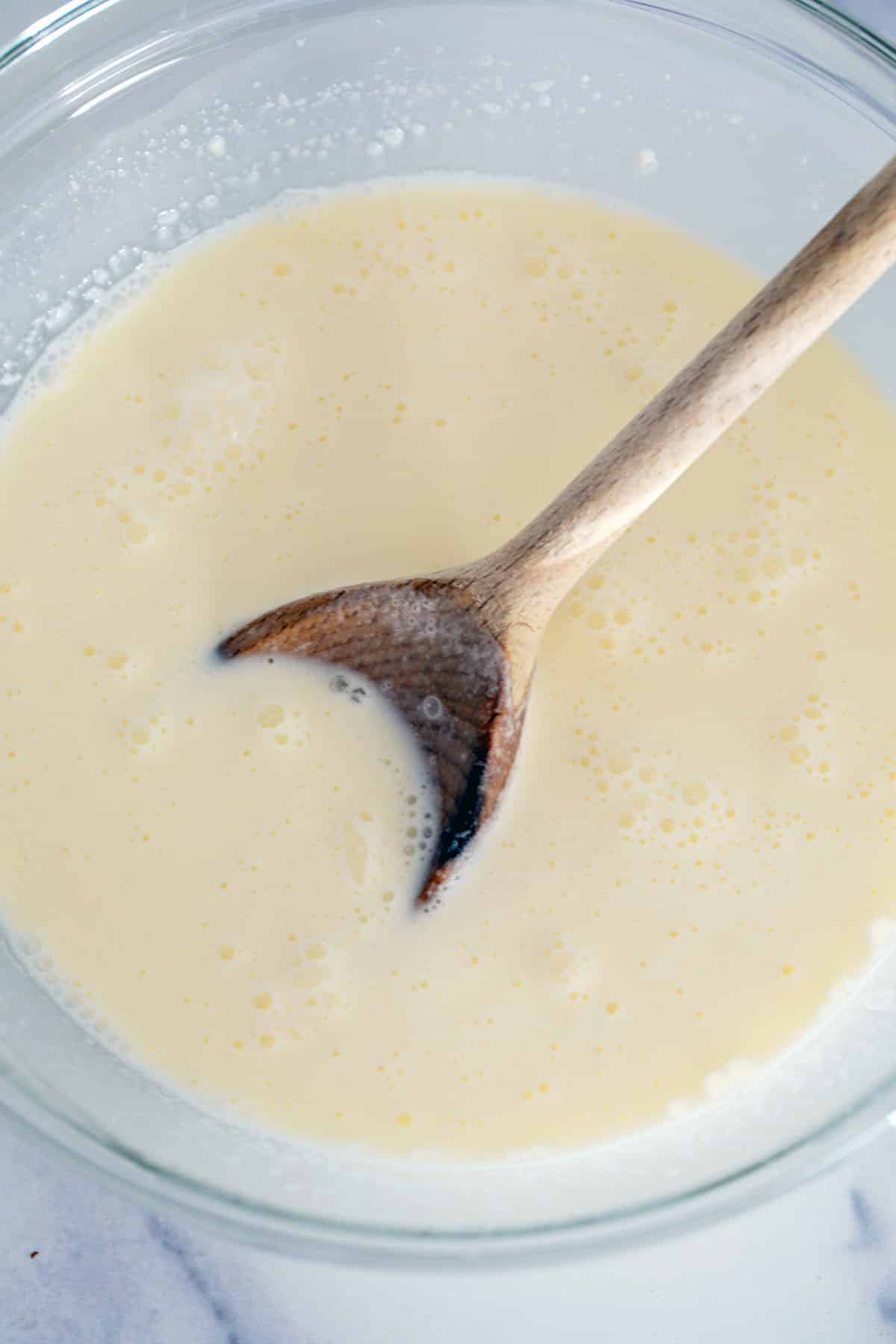 Cream, milk, and sugar stirred together in bowl with wooden spoon.