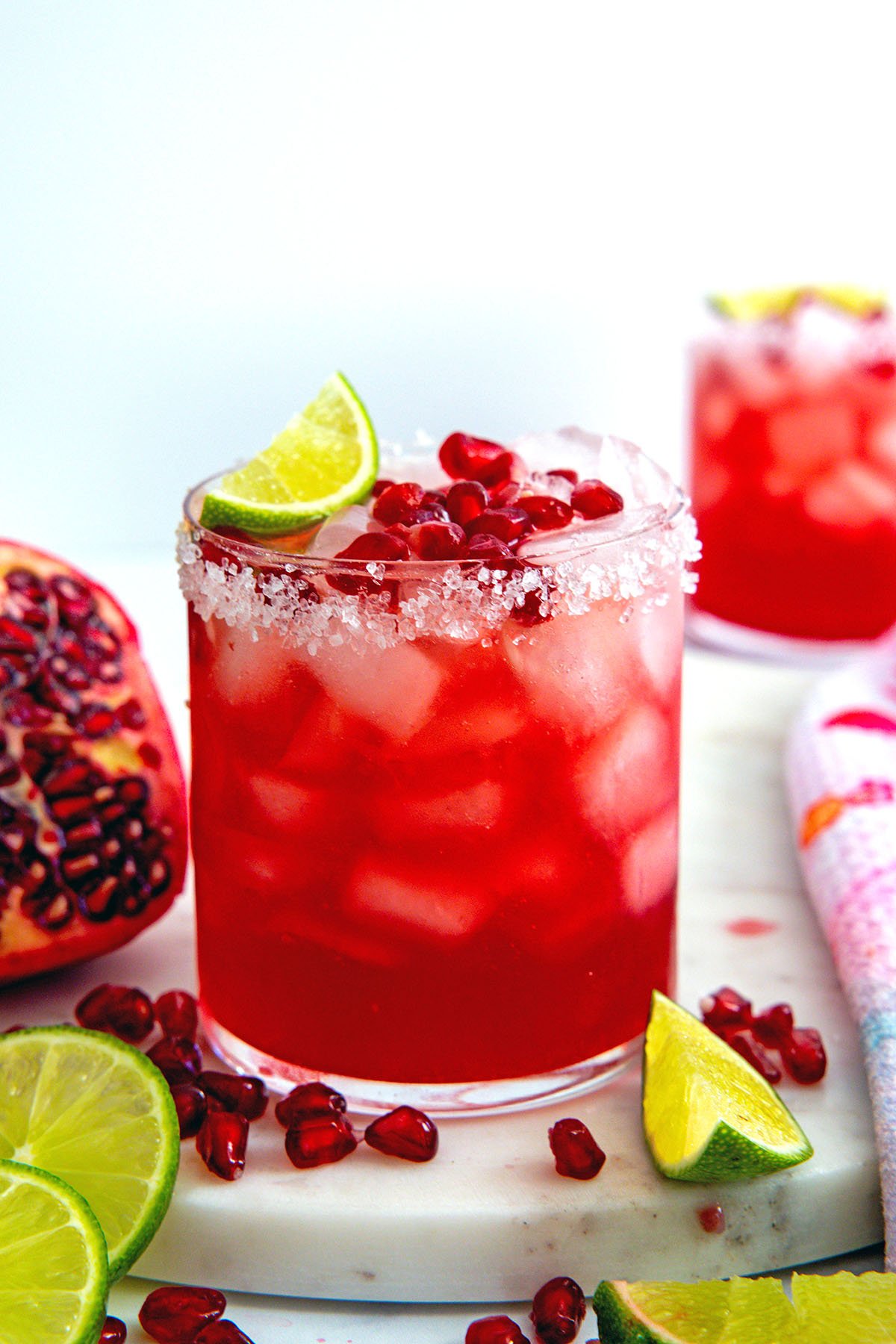 Head-on view of a pomegranate margarita with arils and lime wedges all around.