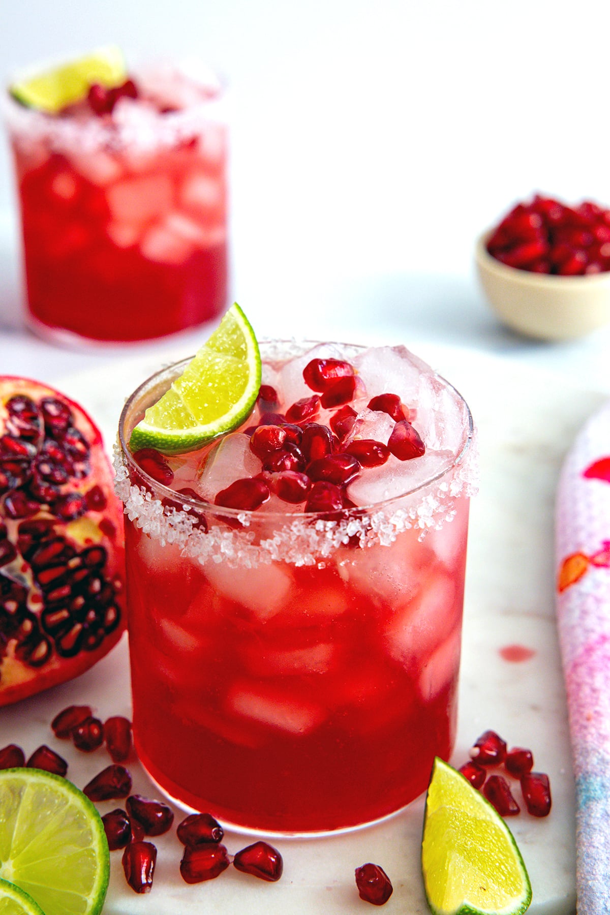 Overhead view of a pomegranate margarita with arils and lime wedge for garnish and second margarita in the background.