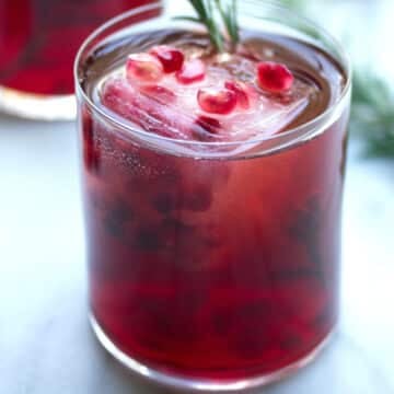 Closeup view of a pomegranate rosemary sparkler with pom arils and rosemary sprig garnish.