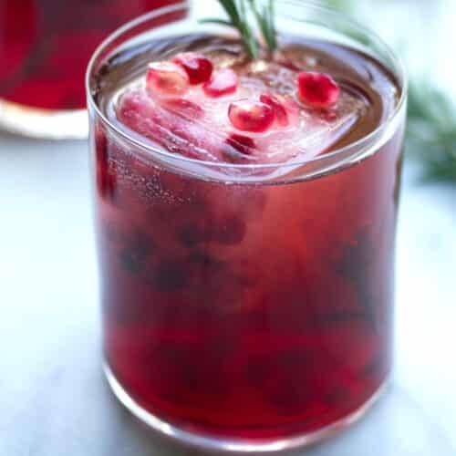 Closeup view of a pomegranate rosemary sparkler with pom arils and rosemary sprig garnish.