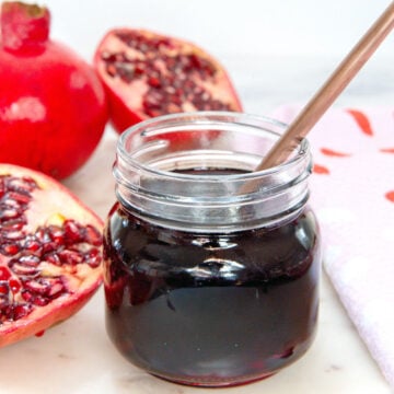 Closeup view of a small jar of pomegranate syrup with pomegranate halves.