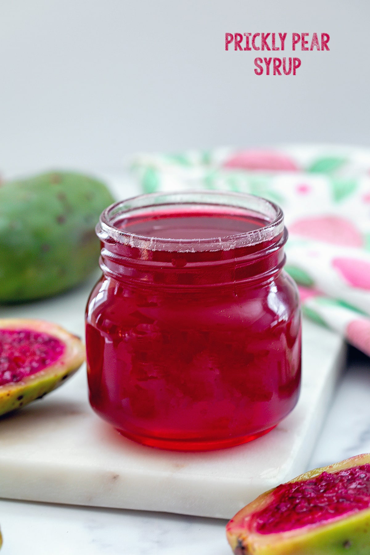 Small jar of prickly pear syrup with fresh prickly pears in background and recipe title at top.