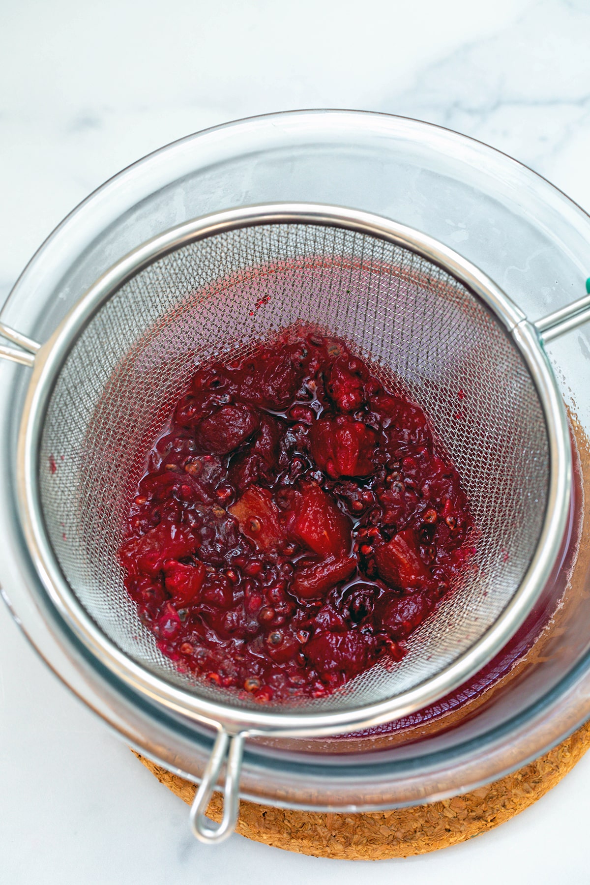 Prickly pear flesh being strained out of syrup into bowl.