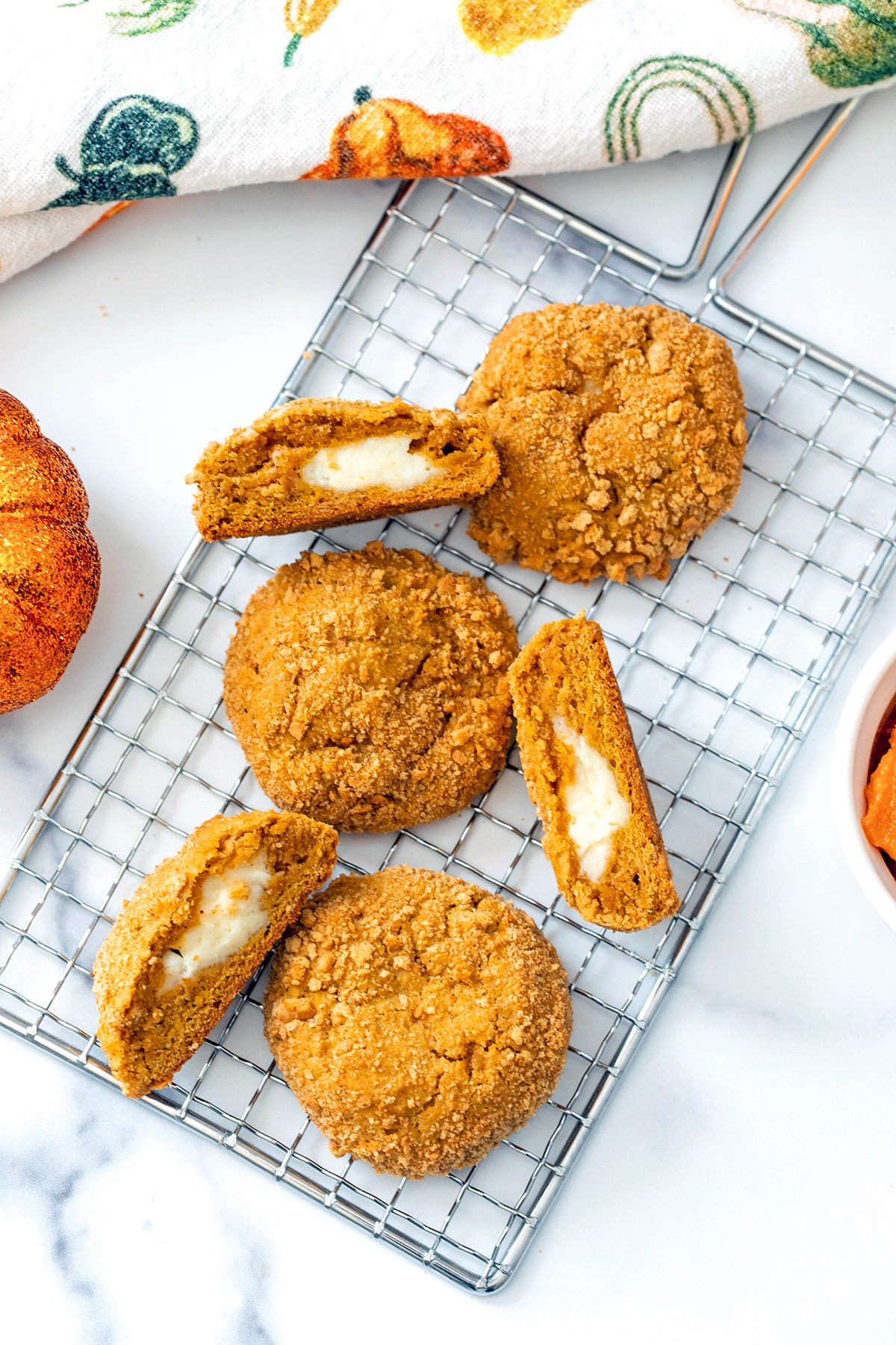 Overhead view of pumpkin cheesecake cookies on metal rack, some cookies cut in half to show cheesecake centers.