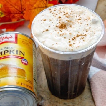Overhead closeup view of the pumpkin cold foam on top of an iced coffee with can of pumpkin puree on the side.