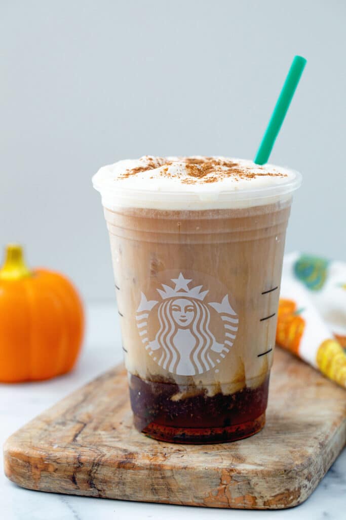 Pumpkin Cream Cold Brew in a Starbucks cup with green straw and small pumpkin in background.