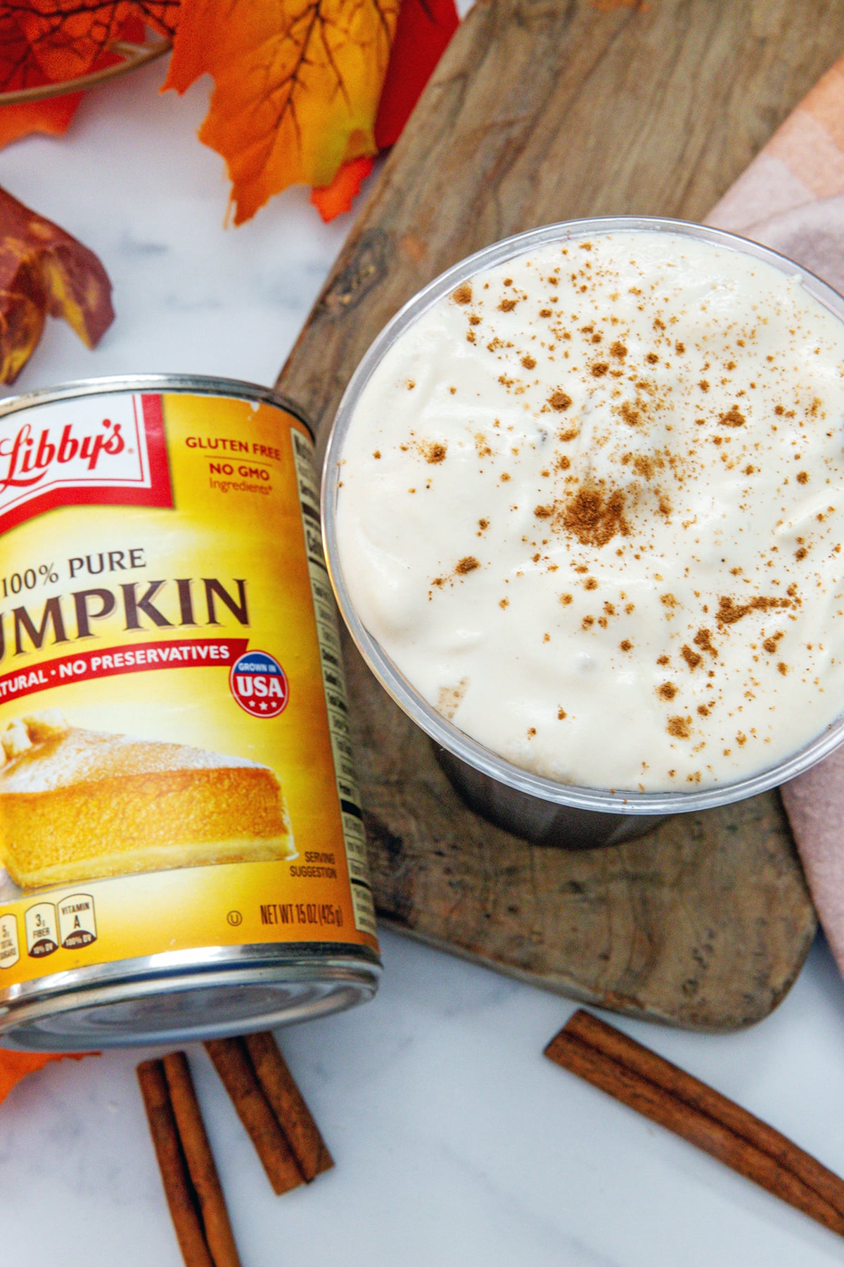 Closeup overhead view of cup of iced coffee topped with pumpkin cold foam with pumpkin pie spice with can of pumpkin on the side.
