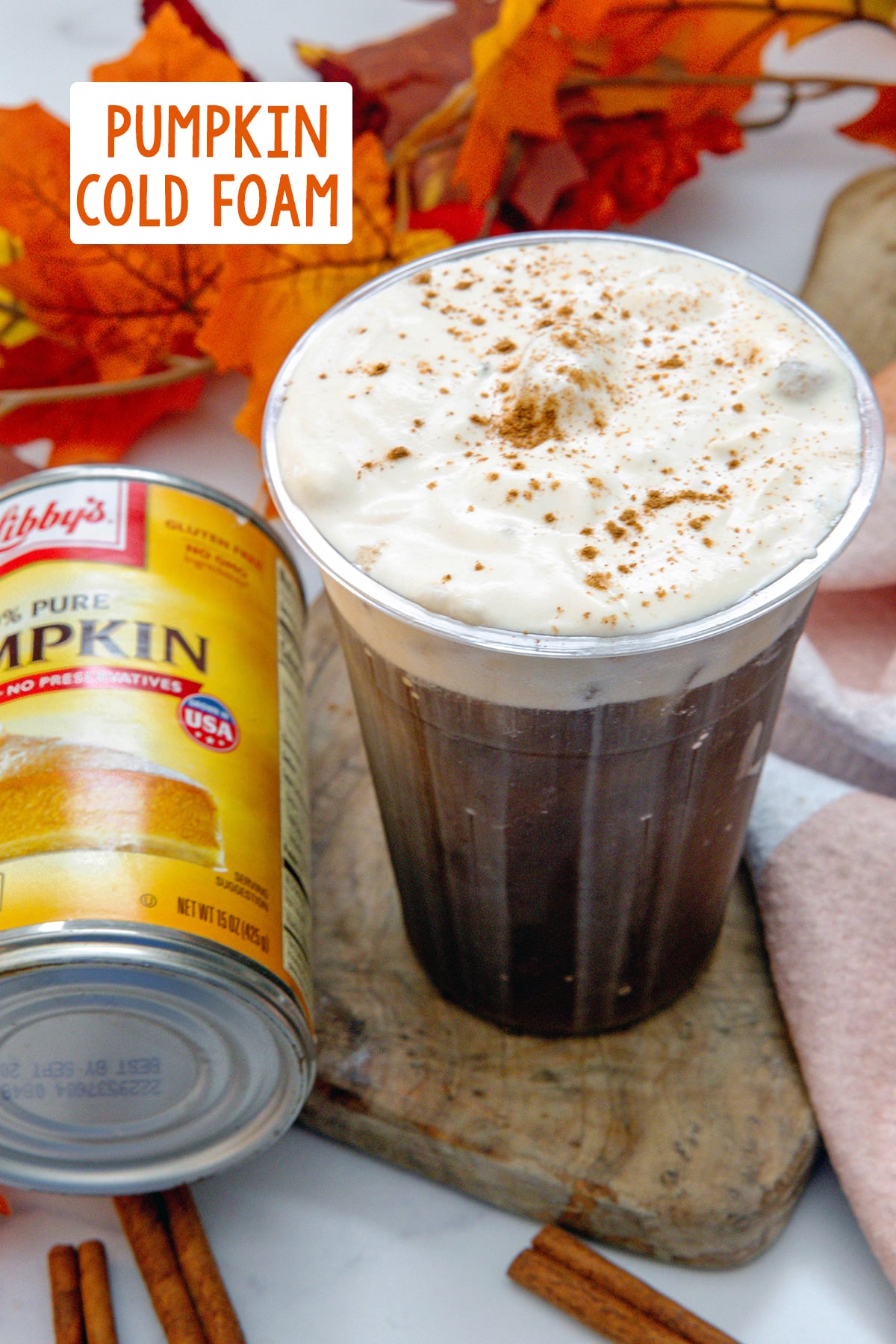 Overhead view of cup of iced coffee topped with pumpkin cold foam with pumpkin pie spice with can of pumpkin on the side and recipe title at top.