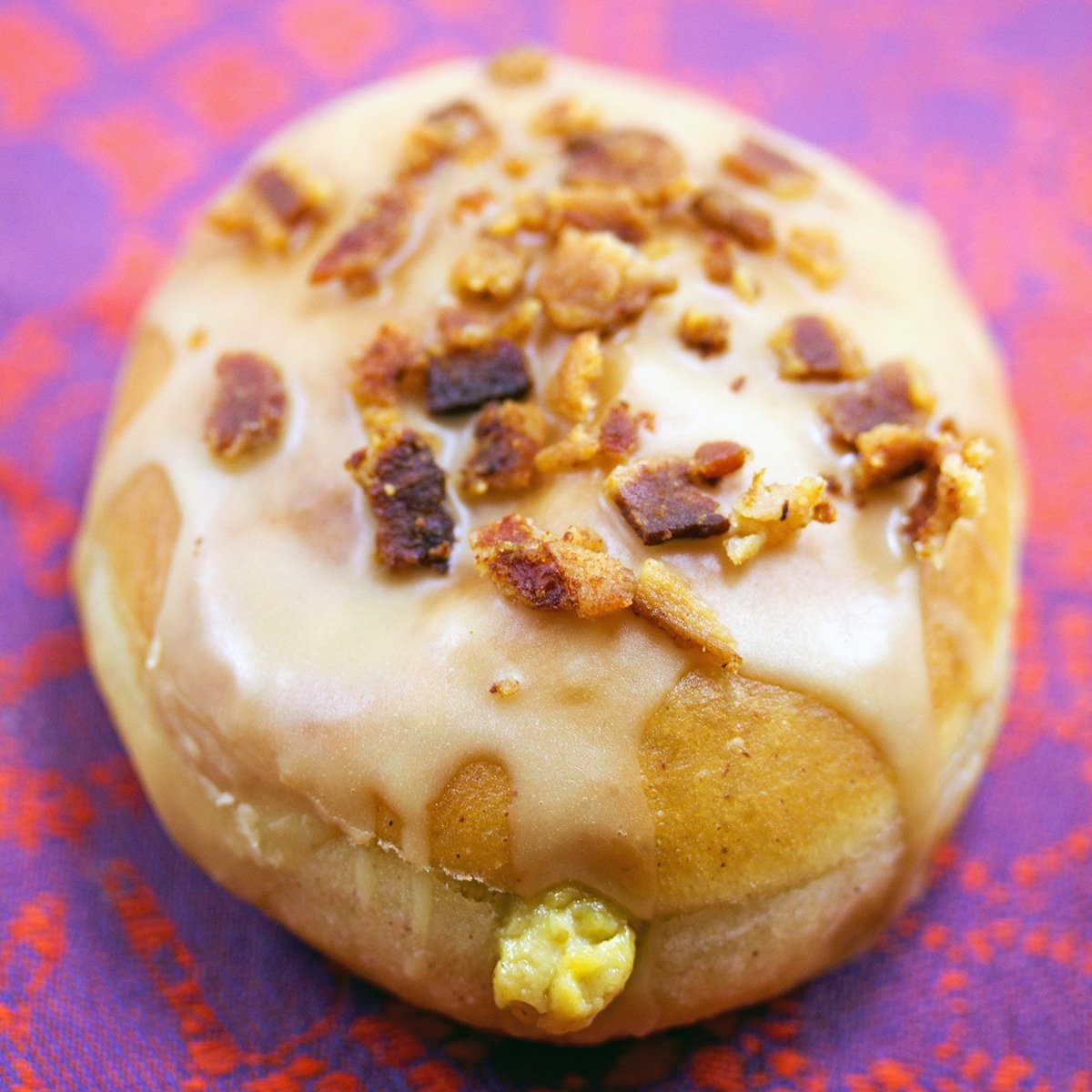 Closeup of a fried donut with pumpkin custard topped with maple bacon frosting.