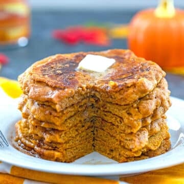 Closeup view of a stack of pumpkin pancakes with piece cut out and butter on top.
