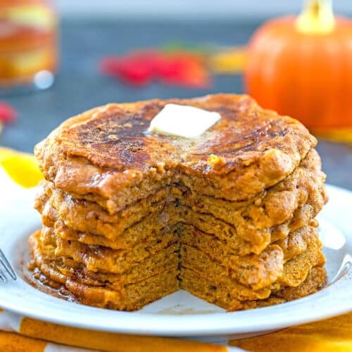 Closeup view of a stack of pumpkin pancakes with piece cut out and butter on top.