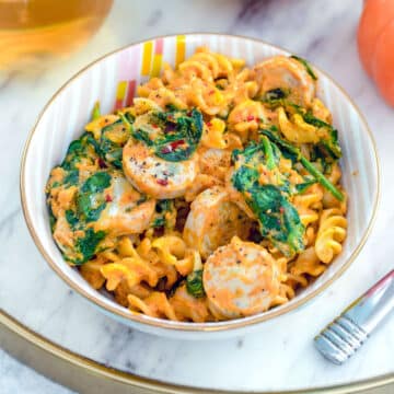 Closeup view of a bowl of pumpkin pasta with chicken sausage and spinach.