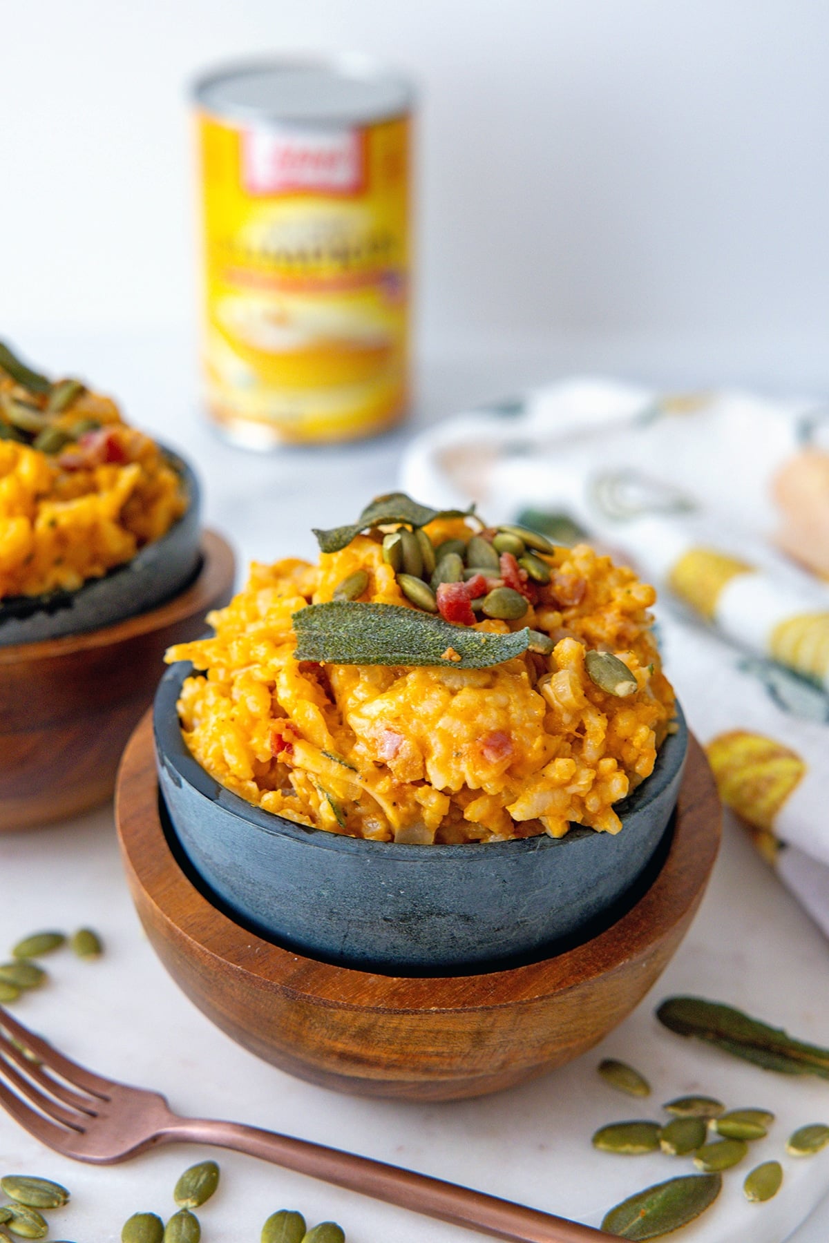 Head-on view of pumpkin risotto in a bowl with can of pumpkin in background and fork in foreground.