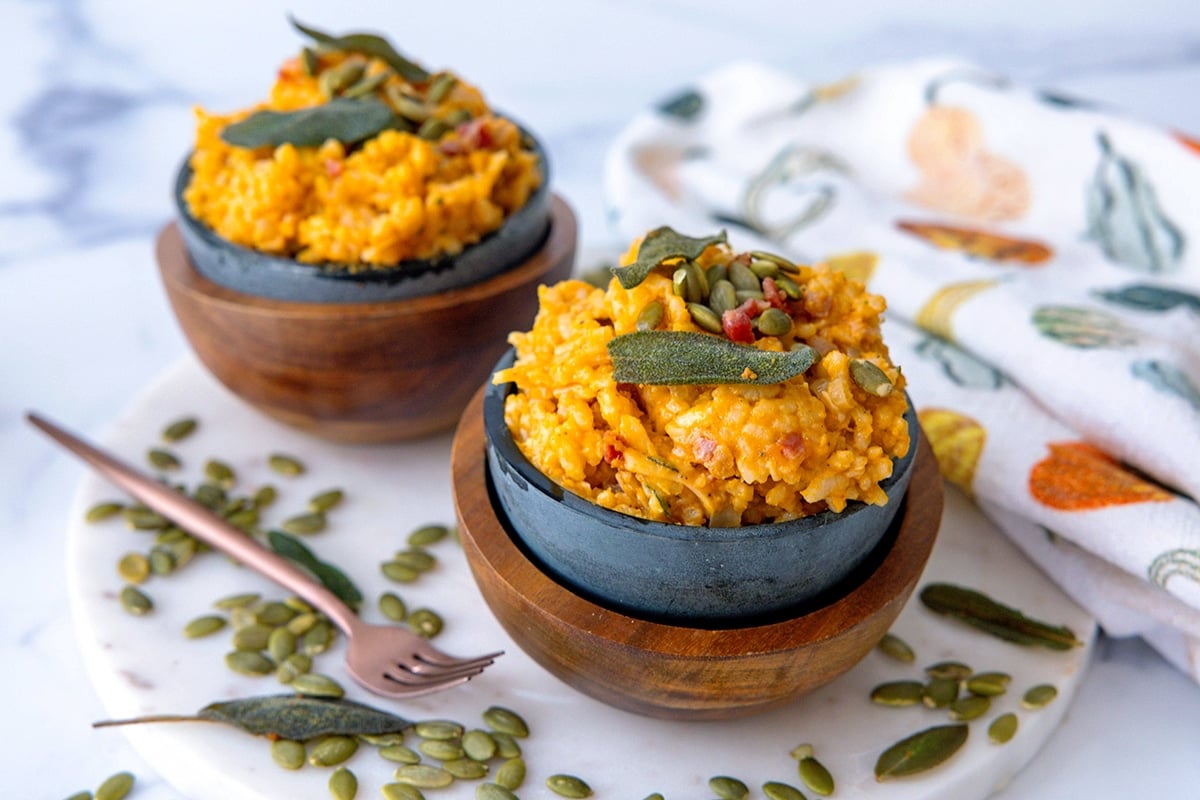 Landscape view of two bowls of pumpkin risotto with pumpkin seeds all around.