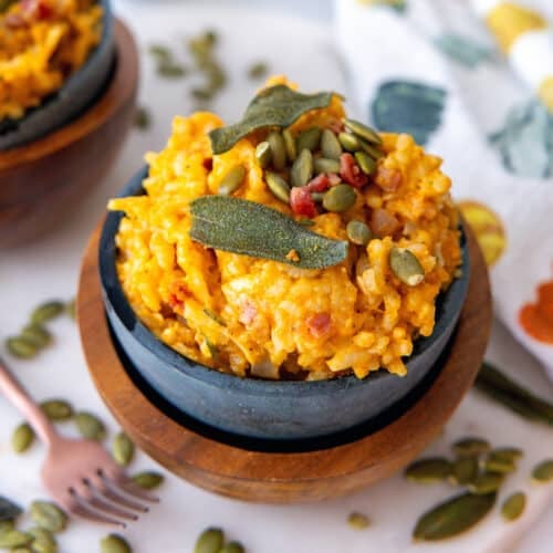 Closeup view of a bowl of pumpkin risotto with pumpkin seeds all around.