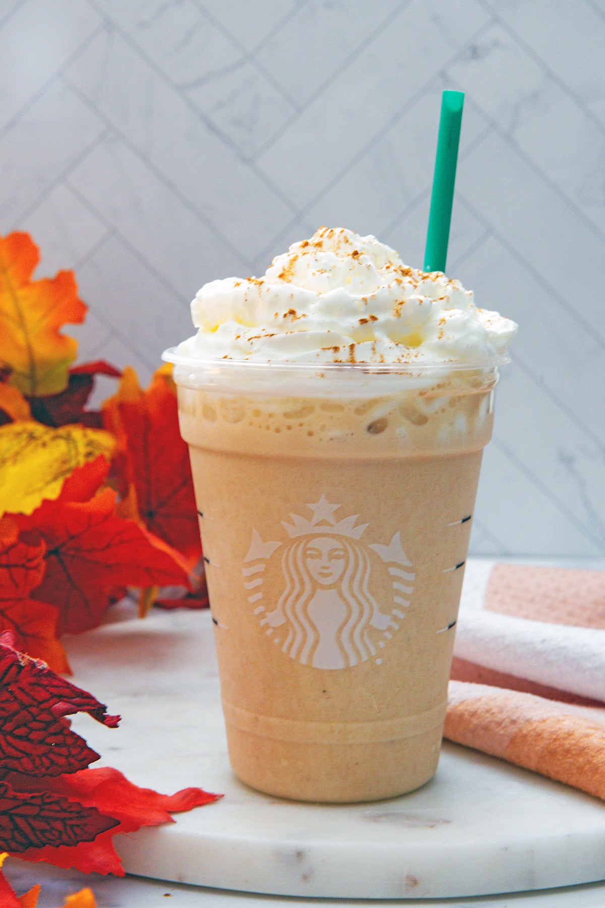 Head-on view of Pumpkin Spice Frappuccino in Starbucks cup with whipped cream and green straw.