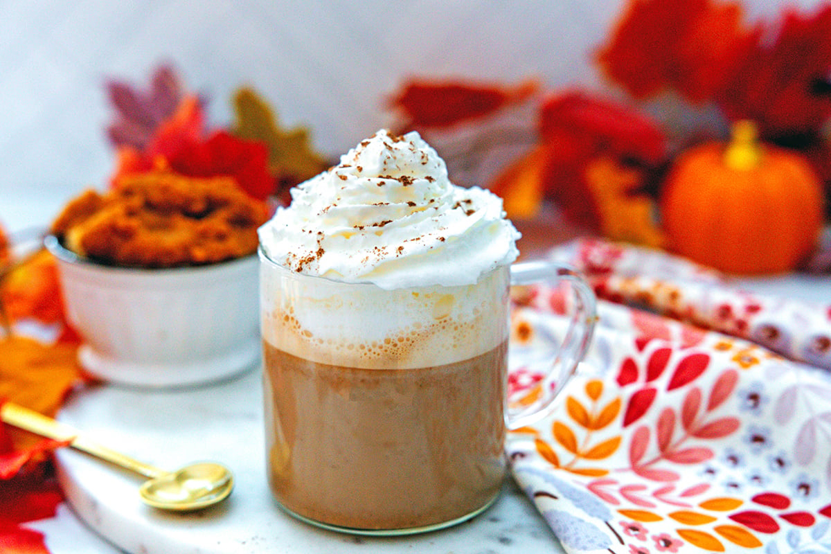 Landscape view of a pumpkin spice latte with whipped cream with pumpkin puree in background.