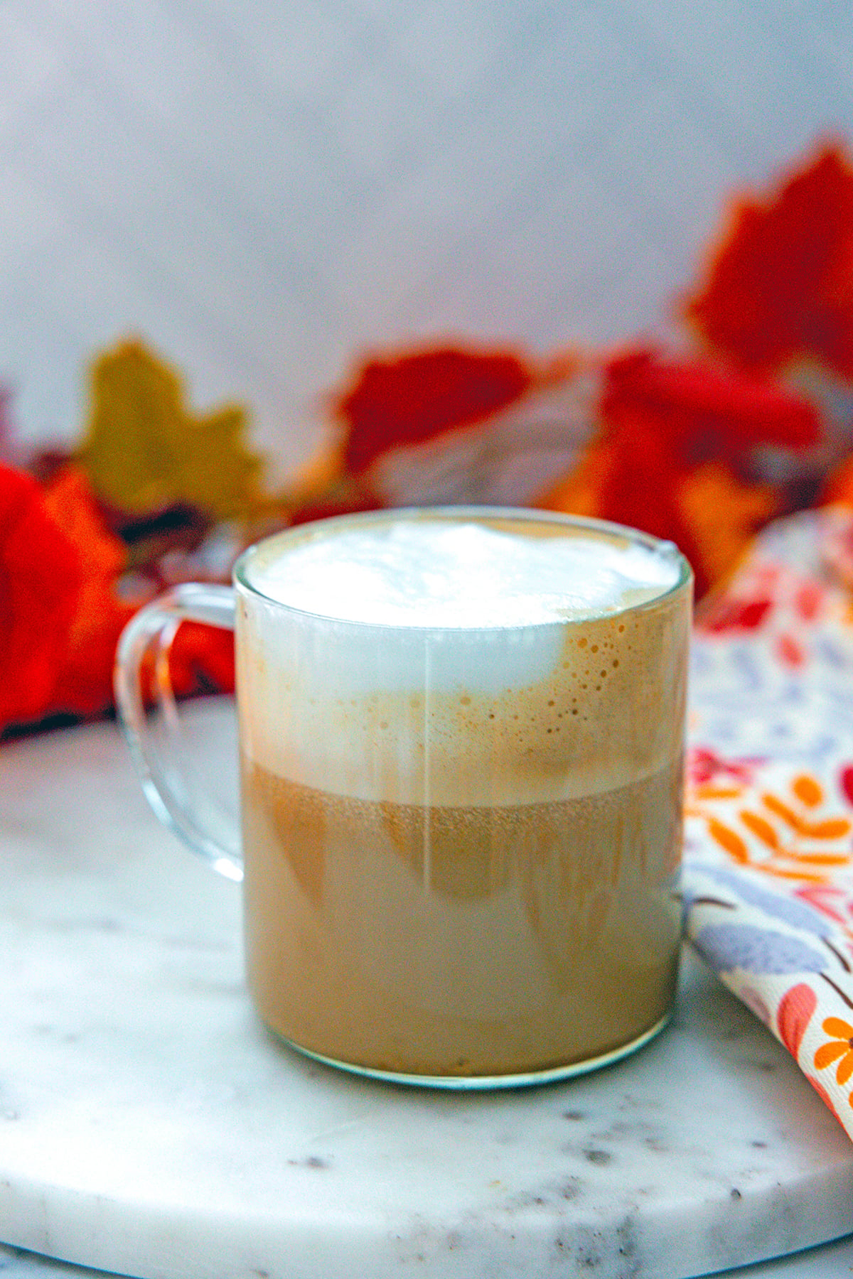 Pumpkin spice latte in clear mug with frothy milk on top.