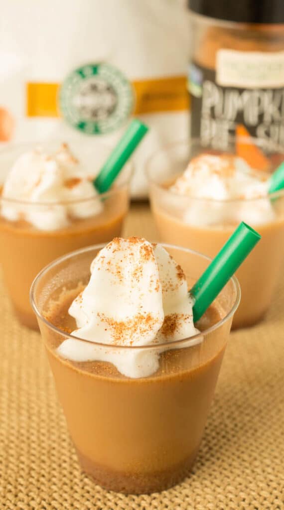Pumpkin latte jello shots in cups with whipped cream and green straws
