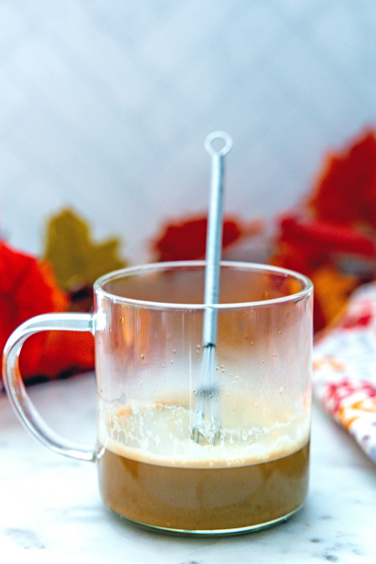 Head-on view of coffee mug with espresso and pumpkin pie sauce and a small whisk.