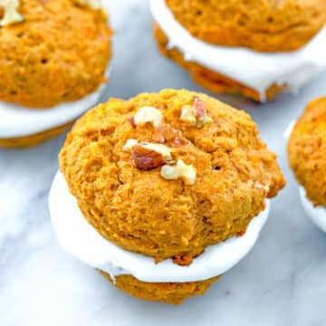 Closeup of a pumpkin whoopie pie with walnuts on top and more whoopie pies in background.
