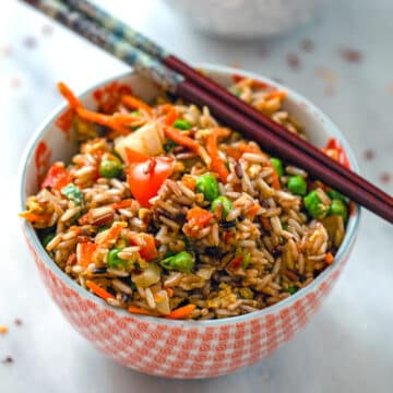 Closeup view of a bowl of vegetable fried rice with chopsticks.