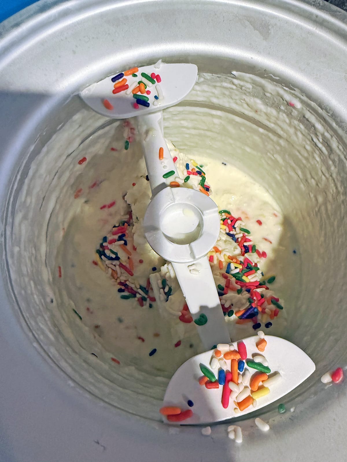 Rainbow sprinkles being processed into ice cream in maker.