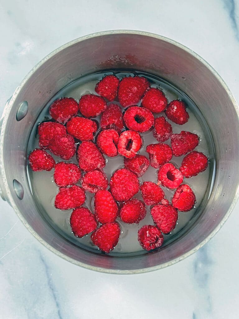 Fresh raspberries in saucepan with water and sugar.