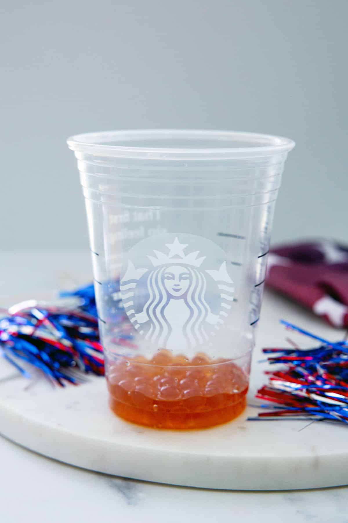 Head-on view of a Starbucks cup with raspberry boba pearls on the bottom.