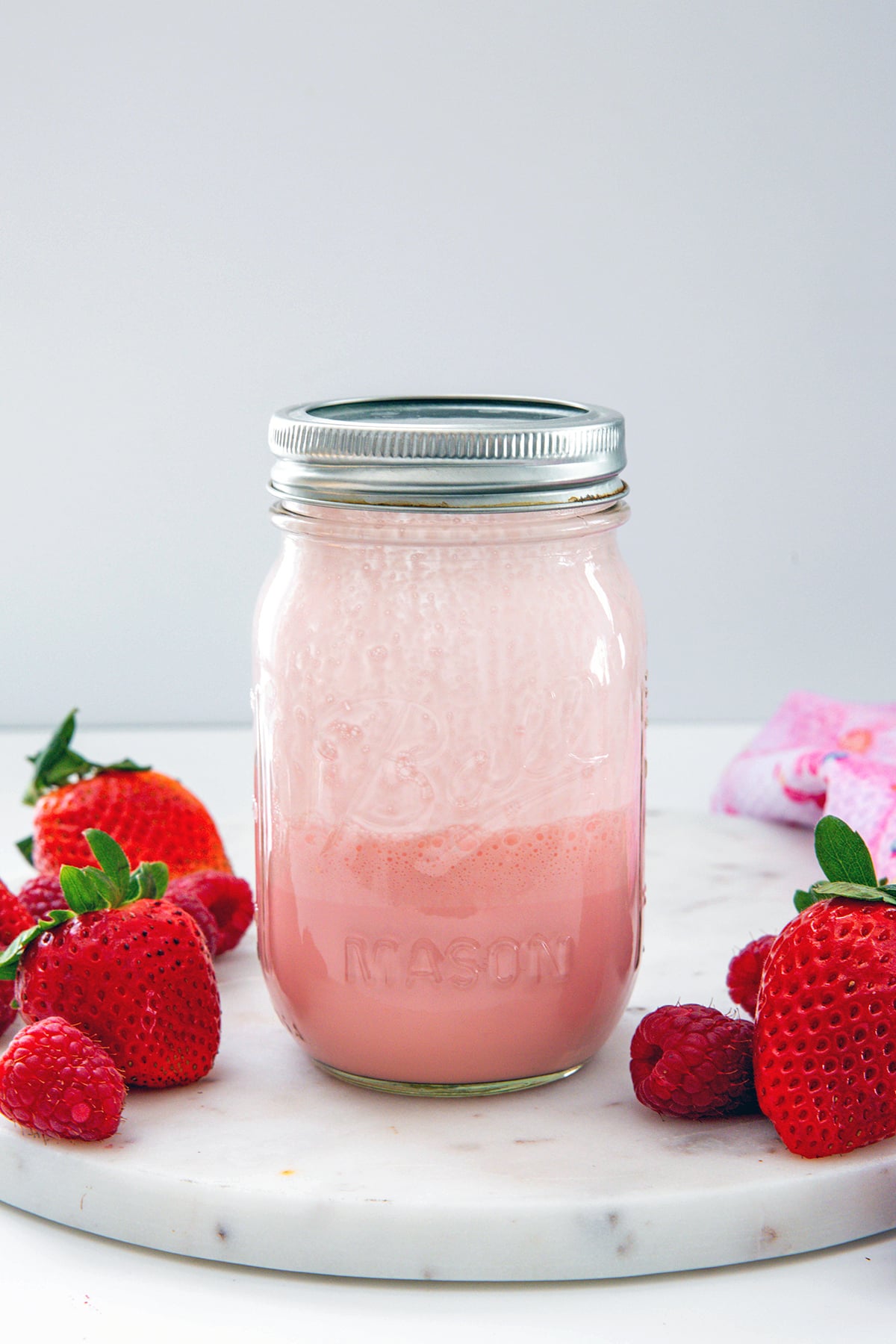 Mason jar with raspberry cold cream with strawberries all around.