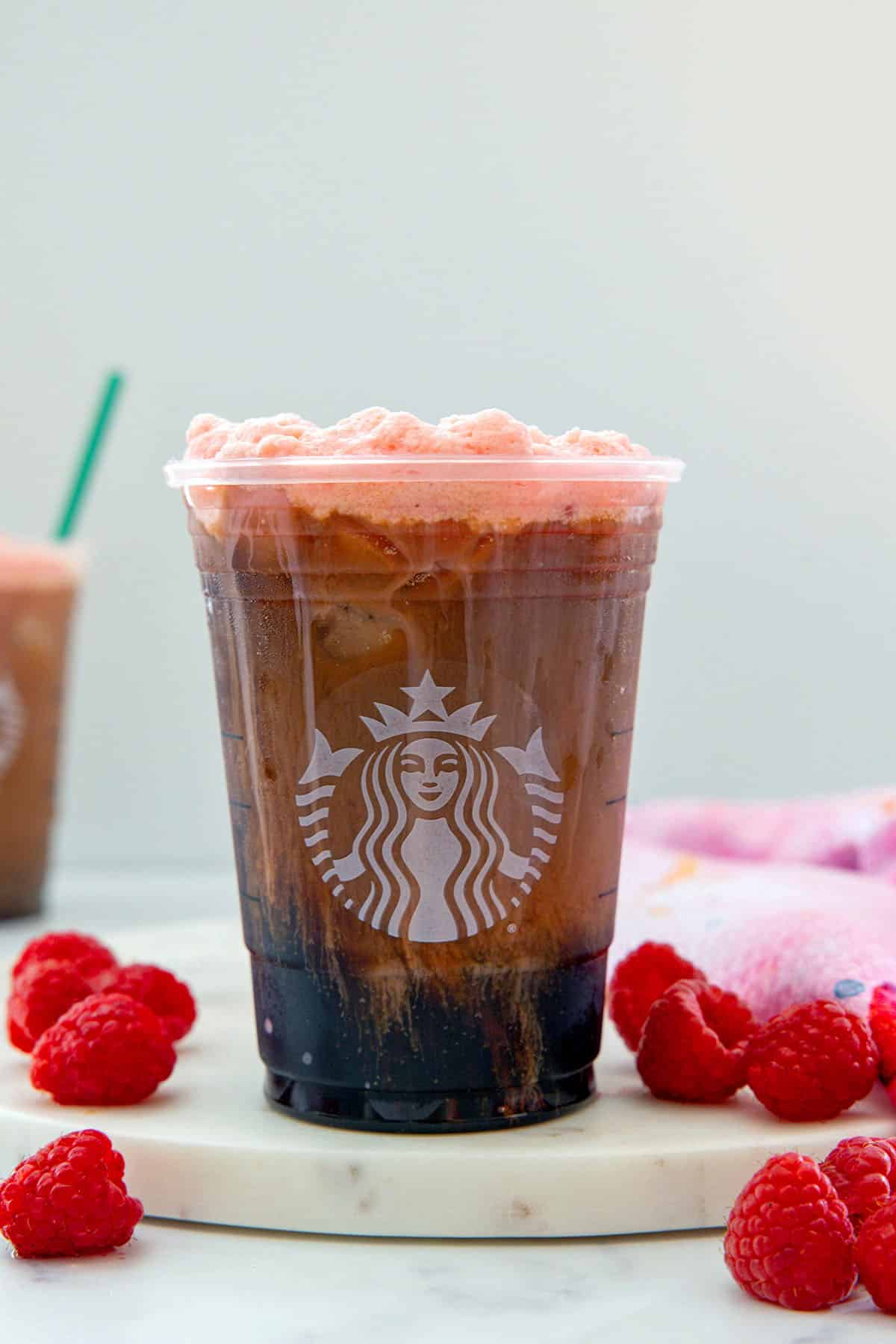 Head-on view of a raspberry cream cold brew with raspberry cold foam and fresh raspberries all around.